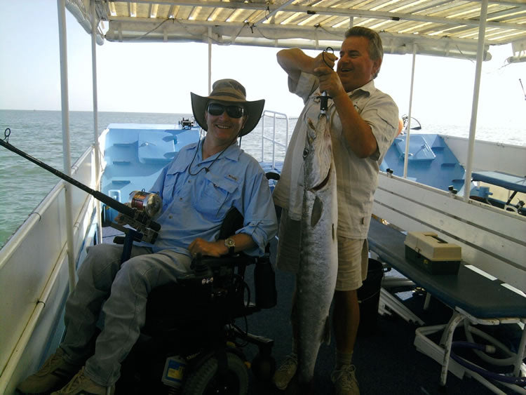 Adaptive fishing quadriplegic man in power wheelchair on boat with huge fish